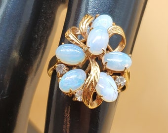 May include: A gold ring with a cluster of oval-shaped white opals and small clear diamonds set in a floral design.