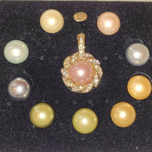 May include: A set of nine pearls in a velvet box. The pearls are in various shades of white, pink, and gold. The pearls are arranged in a circle around a pearl pendant with a gold setting and diamond accents.