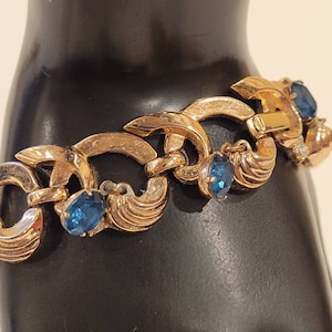 Pulsera vintage Crown Trifari en tono dorado con diamantes de imitación azules colgantes y detalles de diamantes de imitación en las orejas.