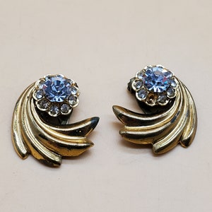 May include: A pair of gold tone clip-on earrings with a blue rhinestone centre surrounded by clear rhinestones.