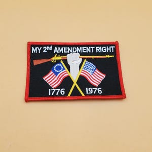 May include: Black rectangular patch with red edging, displaying the text "MY 2nd AMENDMENT RIGHT". The patch features a rifle, a raised fist, and crossed flags of the United States and Georgia. The dates "1776" and "1976" are also included.