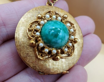 Puede incluir: Un collar de oro con un medallón con un camafeo verde y un borde de perlas. El medallón está abierto y tiene una superficie texturizada.