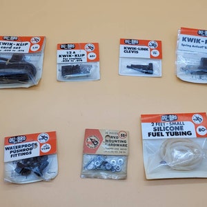 May include: A collection of seven small plastic bags containing various model airplane parts and accessories. The bags are labeled with the brand name "DU-BRO" and the names of the products, such as "KWIK-KLIP", "WATERPROOF PUSHROD FITTINGS", and "SILICONE FUEL TUBING".