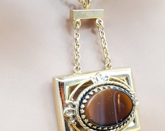 May include: A gold chain necklace with a square pendant featuring a brown oval stone set in a gold frame.