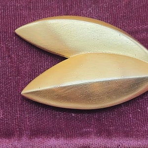 May include: A gold-colored metal brooch in the shape of two overlapping leaves.