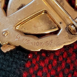 Puede incluir: Primer plano de un broche de metal dorado con la inscripci&oacute;n "1/5-10K-G.F."