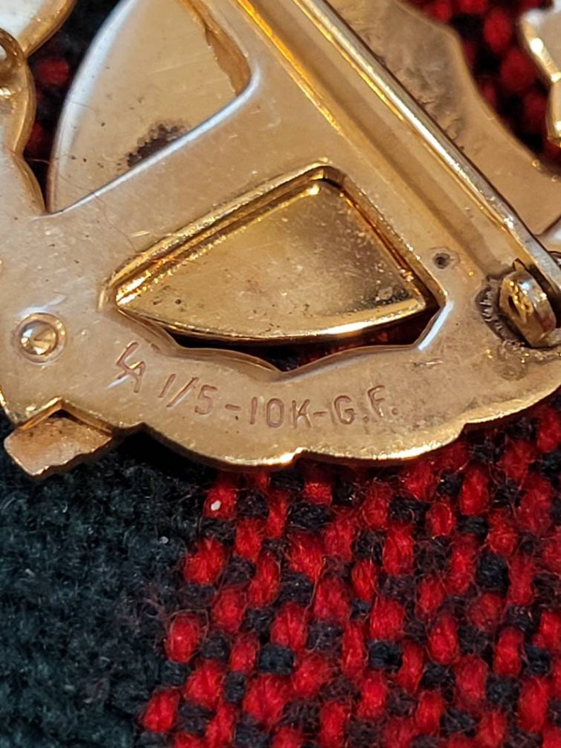 Puede incluir: Primer plano de un broche de metal dorado con la inscripci&oacute;n "1/5-10K-G.F."