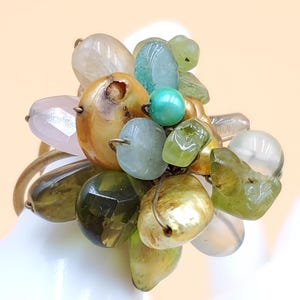 May include: A cluster ring featuring a variety of colorful beads in shades of green, gold, blue, and clear. The beads are clustered together, creating a unique and eye-catching design. The ring has a gold-tone band.