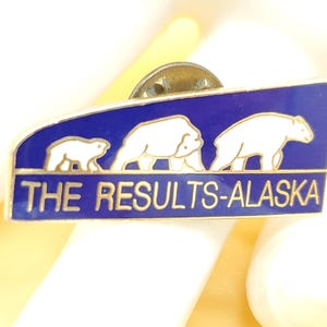 Puede incluir: Pin rectangular con fondo azul y tres osos polares blancos. El texto "THE RESULTS-ALASKA" está en letras doradas. El pin tiene un respaldo de metal dorado.
