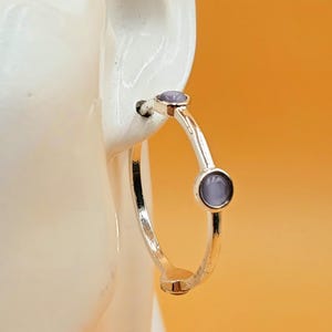 Puede incluir: Pendientes de aro de plata con dos pequeñas piedras de color morado claro.