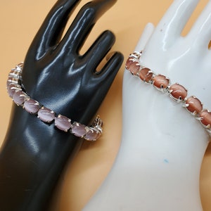 May include: Two bracelets with oval-shaped stones. One bracelet has light pink stones and the other has brown stones.