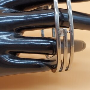 Puede incluir: Pulsera de plata con tres bandas y un pequeño acento de piedra clara.