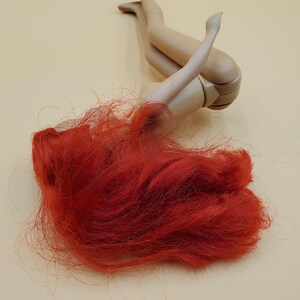 May include: A red haired doll laying on its back with its legs in the air. The doll is made of plastic and has a simple design.