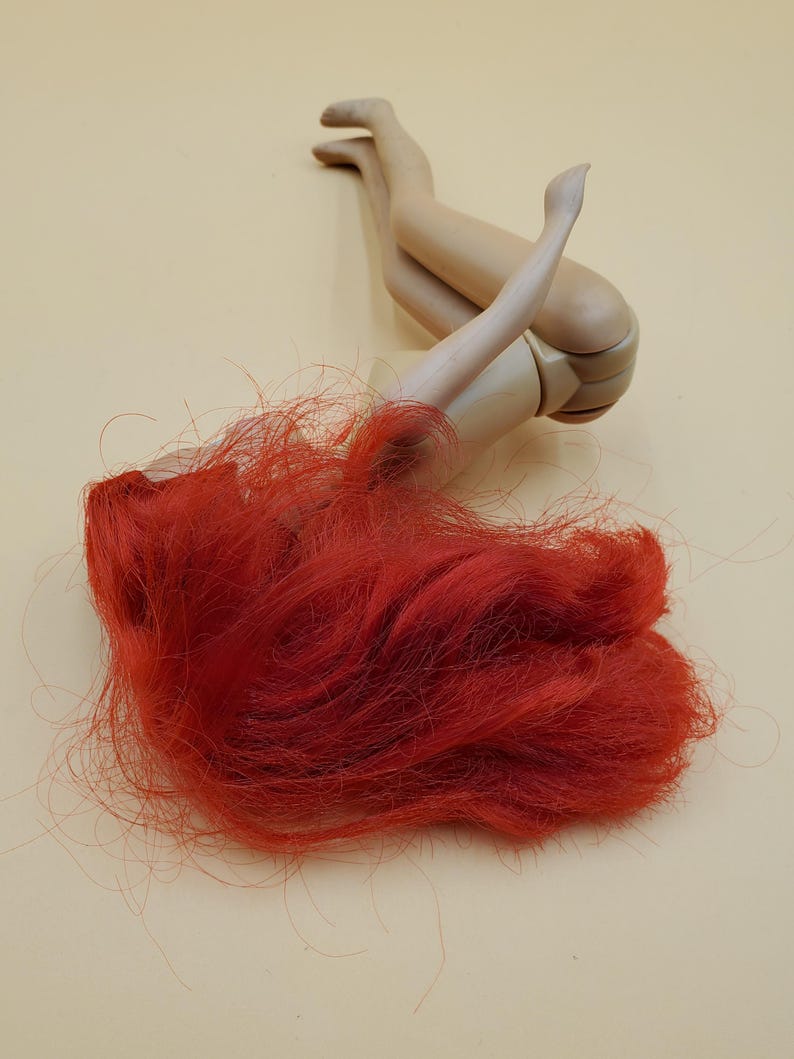 May include: A red haired doll laying on its back with its legs in the air. The doll is made of plastic and has a simple design.