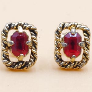 May include: A pair of vintage stud earrings. Each earring features a rectangular, faceted, deep red gemstone set within a gold-toned, twisted rope-like frame. The earrings have a classic, elegant design.