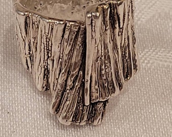 May include: A silver ring with a textured, tree bark-like design.