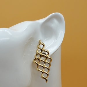 May include: Gold-toned geometric dangle earrings with a woven design. The earrings are displayed on a white mannequin head.