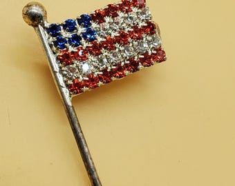 May include: A silver pin with a red, white and blue rhinestone American flag.