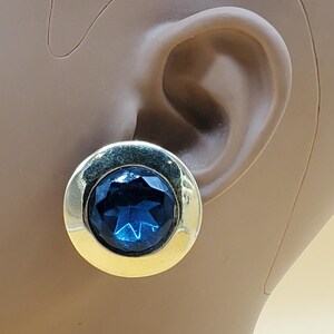 May include: A pair of gold tone earrings with a large, dark blue, faceted gemstone in the center of each earring.