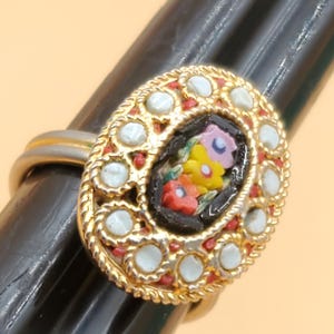 May include: Gold-toned ring with an oval mosaic design. The mosaic features a floral pattern with red, yellow, and pink flowers on a black background. The ring is accented with white and red details.