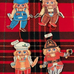 May include: Set of four wooden nutcracker ornaments. Each ornament features a different profession: carpenter, cowboy, chef, and firefighter. The ornaments are painted in bright colors and have a whimsical design. Made in Taiwan.