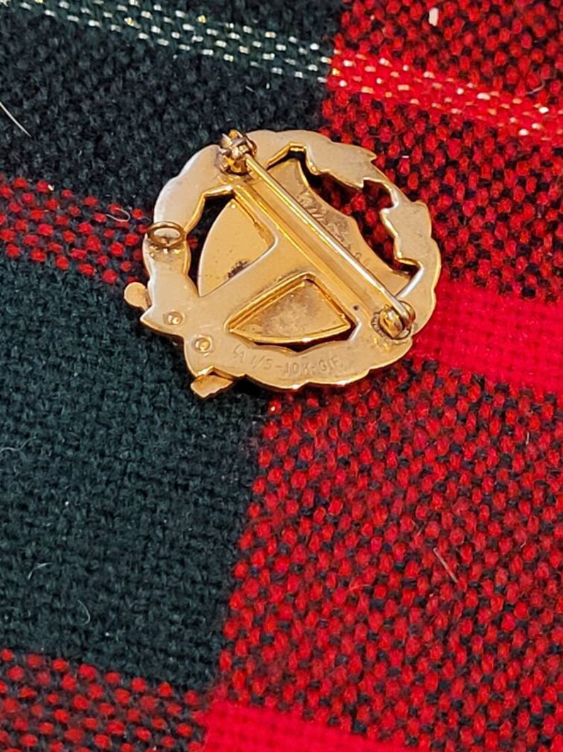 Puede incluir: Pin de tono dorado con un dise&ntilde;o de corona y un escudo central. La parte posterior del pin tiene la inscripci&oacute;n "9/1/45 - 10/2/45 GF".