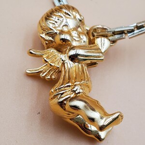 Pu&ograve; includere: Un ciondolo a forma di cherubino dorato con ali spiegate e un arco. Il cherubino &egrave; attaccato a una catena color argento. Il ciondolo &egrave; molto dettagliato e ha una finitura lucida.