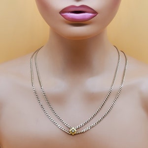 May include: A silver chain necklace with a gold square pendant featuring a small clear stone. The necklace is layered with two chains.