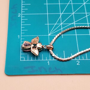May include: A gold-toned pendant necklace with a floral design. The pendant features a cluster of petals with a central purple gemstone. The chain is a silver-coloured, textured link style. The pendant measures approximately 2.5 cm in length.