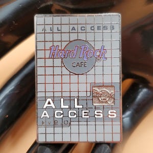 May include: A rectangular Hard Rock Cafe pin with a grey grid pattern. The pin features the Hard Rock Cafe logo in purple and the words "ALL ACCESS" in white. A smaller Hard Rock Cafe logo is in the upper right corner.