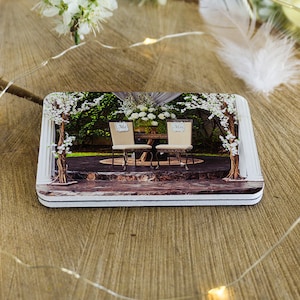 May include: Two white chairs with signs that say "Mr." and "Mrs." are set up under a floral archway. The chairs are on a stone patio with a green lawn in the background.