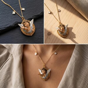 Puede incluir: Collar dorado con un colgante con dise&ntilde;o de querub&iacute;n. El querub&iacute;n tiene alas blancas y est&aacute; enmarcado en un &oacute;valo. El collar tambi&eacute;n tiene peque&ntilde;os adornos blancos. El collar se muestra sobre una superficie negra, una superficie de madera y siendo usado.
