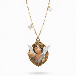 Puede incluir: Un collar dorado con un colgante con un dise&ntilde;o de querub&iacute;n. El querub&iacute;n tiene alas blancas y est&aacute; enmarcado en un &oacute;valo. El collar tambi&eacute;n incluye peque&ntilde;os dijes de paloma blancos suspendidos de la cadena.
