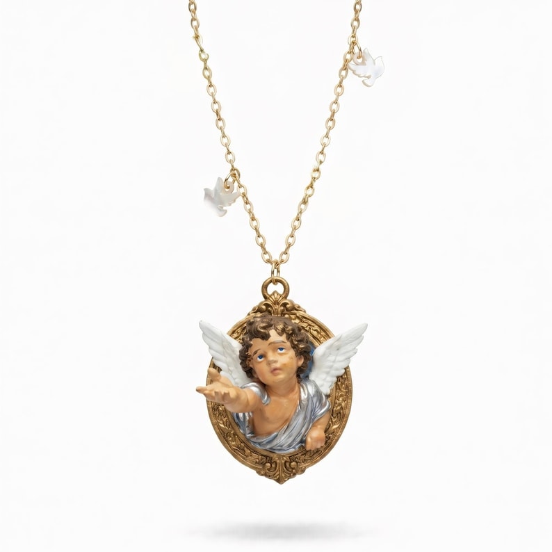 Puede incluir: Un collar dorado con un colgante con un dise&ntilde;o de querub&iacute;n. El querub&iacute;n tiene alas blancas y est&aacute; enmarcado en un &oacute;valo. El collar tambi&eacute;n incluye peque&ntilde;os dijes de paloma blancos suspendidos de la cadena.