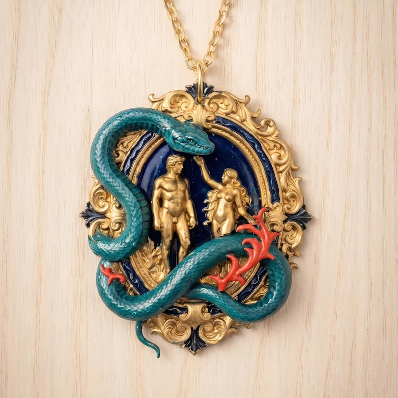 May include: A gold-toned pendant necklace featuring a teal snake coiled around a framed scene of two figures. The frame has a blue background and gold accents. Red coral-like details add contrast.