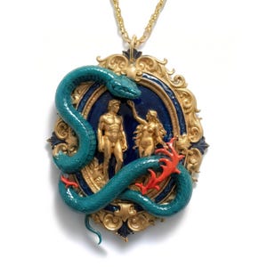 May include: Gold-toned pendant necklace featuring a teal snake coiled around a framed scene of Adam and Eve. The frame is gold with a dark blue background, and the figures are gold. The snake has red accents.