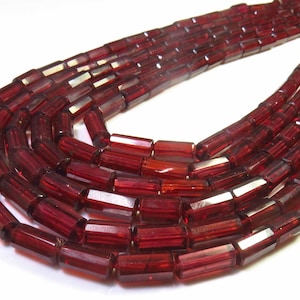 Op de afbeelding: Close-up van meerdere strengen diep bordeauxrode, rechthoekige kralen. De kralen zijn facetgeslepen en doorschijnend, waardoor ze licht reflecteren. Ze zijn geregen, geschikt voor het maken van sieraden of andere knutselwerkjes.