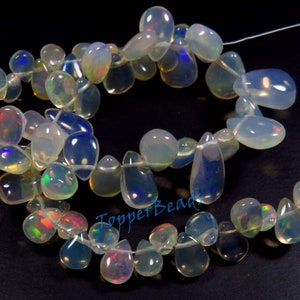 May include: Strands of iridescent opal beads in various teardrop and oval shapes. The opals display a range of colors, including blue, green, and red, with a translucent, milky appearance. The beads are strung on a thin, clear cord.