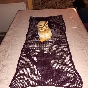 Może przedstawiać: Fioletowy, haftowany bieżnik stołowy z figurką sowy w środku. Bieżnik ma powtarzający się wzór sów.