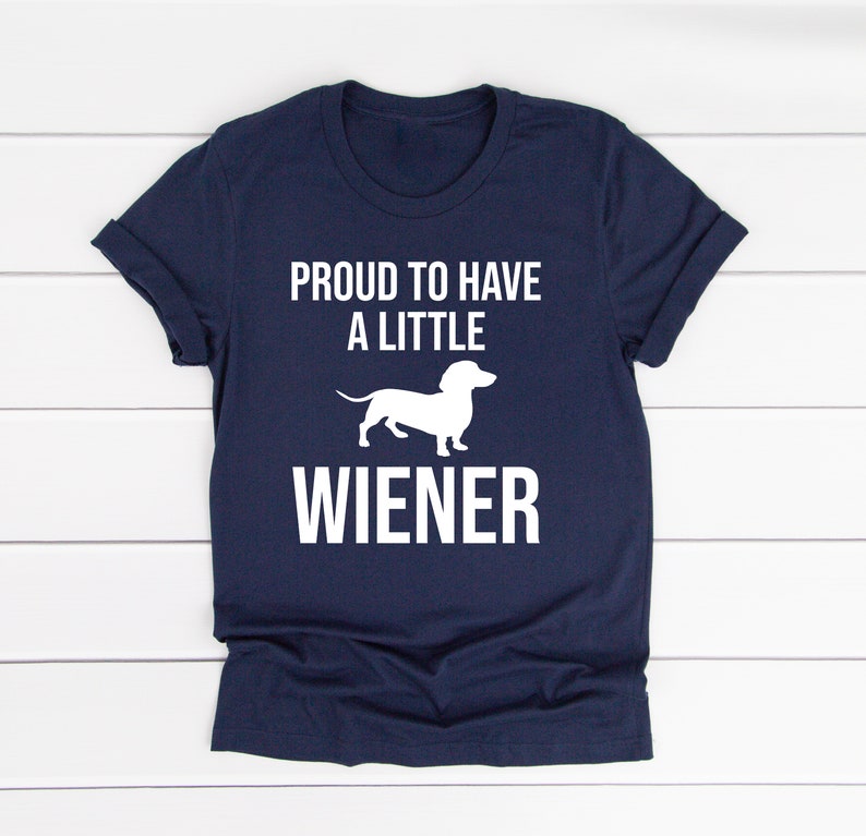 May include: A navy blue t-shirt with white text that reads "Proud to have a little wiener" and a white silhouette of a dachshund.