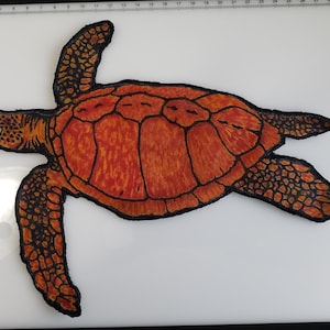 May include: An orange and black sea turtle illustration. The turtle is drawn with detailed lines, showcasing its shell pattern and flippers. The artwork is set against a white background, highlighting the vibrant colors of the sea creature.
