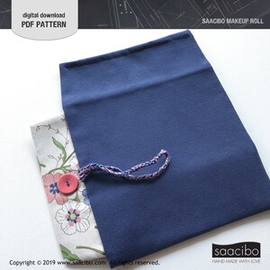 Pu&ograve; includere: Un astuccio per il trucco blu navy con interno a fantasia floreale. Il rotolo &egrave; fissato con un bottone rosa e un cordoncino intrecciato. Il testo "SAACIBO MAKEUP ROLL" &egrave; visibile. L'immagine include anche il testo "digital download PDF PATTERN".