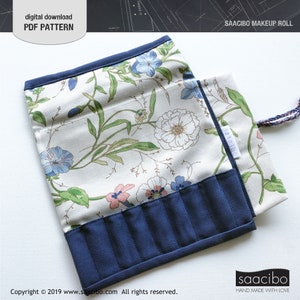 Pu&ograve; includere: Un astuccio per il trucco con stampa floreale con base e finiture blu navy. Il rotolo presenta uno sfondo color crema con fiori blu, rosa e bianchi e foglie verdi. Il testo "SAACIBO MAKEUP ROLL" &egrave; visibile. Sono visibili anche le parole "digital download PDF PATTERN".