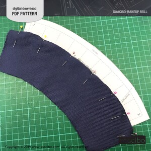 Pu&ograve; includere: Un pezzo di tessuto blu navy appuntato a un modello di carta con l'etichetta "SAACIBO MAKEUP ROLL" e "F-BRUSH DIVIDERS". Il modello &egrave; su un tappetino da taglio verde. Il testo nell'immagine recita "digital download PDF PATTERN".
