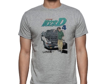 May include: A grey t-shirt featuring a graphic of a white car with its bonnet open and a person standing beside it. The text "Initial D 4" is printed in blue and white on the shirt. The text "Shigeta's First" is printed in black at the bottom of the graphic.
