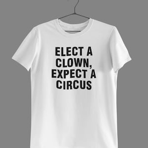 Può includere: Maglietta bianca con testo nero che dice "Eletto un clown, aspettati un circo."