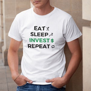 Op de afbeelding: Wit T-shirt met zwarte tekst die "EAT SLEEP INVEST REPEAT" luidt met een vork- en mes-symbool, een slapend gezicht, een dollarteken en een vernieuwsymbool.