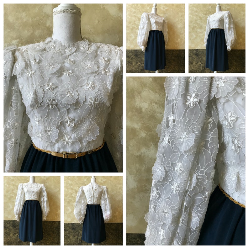 K&ouml;nnte beinhalten: Ein wei&szlig;es Kleid mit einem floralen Spitzenoberteil und einem marineblauen Rock. Das Kleid hat lange &Auml;rmel mit Puff&auml;rmeln und einen goldenen G&uuml;rtel.