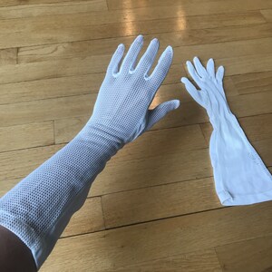 May include: A pair of white long mesh gloves. The gloves are laid out flat on a wooden surface.
