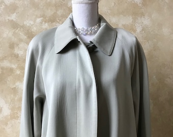 May include: A light green long-sleeved coat with a button closure and a single pocket on the left side. The coat is on a white mannequin with a crystal necklace.